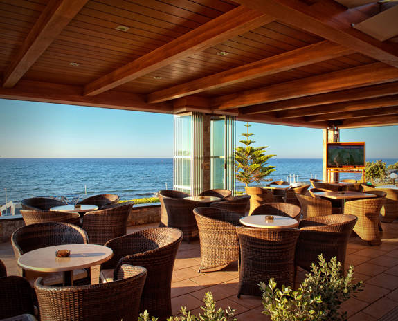 Ariadne Hotel Malia bar sitting area with round tables and armchairs and sea view