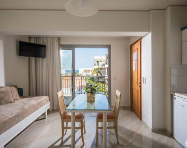 Ariadne Hotel Malia Apartment couch, glass table with decorations and balcony view