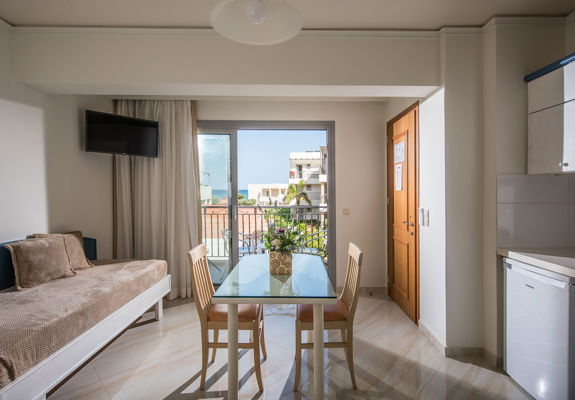 Ariadne Hotel Malia Apartment couch, glass table with decorations and balcony view